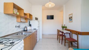 Une cuisine compacte équipée d’une cuisinière à gaz, d’un évier et d’étagères en bois. On y trouve également un coin repas avec une table et des chaises.