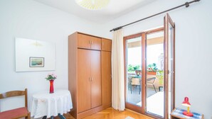 Une pièce avec une armoire en bois, une table ornée d’un vase de fleurs, une chaise et, à travers une porte vitrée, une vue sur un espace extérieur aménagé avec une table et des chaises.