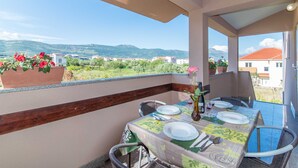 Un balcon avec une table dressée pour le dîner, offrant une vue panoramique sur un paysage magnifique, avec des montagnes et des bâtiments.