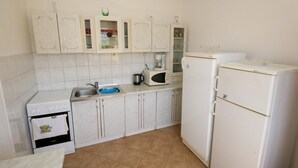 A small kitchen with white cabinets, a sink, a stove, a microwave, and a refrigerator. - Spacious Beachfront Apartment Ciovo (Split)