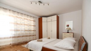 A bedroom with a wooden bed, a nightstand, a wardrobe, and a window with curtains. - Spacious Beachfront Apartment Ciovo (Split)
