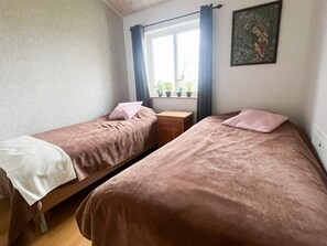 A room with two single beds, a small wooden nightstand, a window with curtains, and a framed picture on the wall. - 4 Star Holiday Home in Bredaryd (Bredaryd)