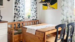 Une table de salle à manger en bois, accompagnée d’un banc, de chaises noires et d’un meuble blanc.
