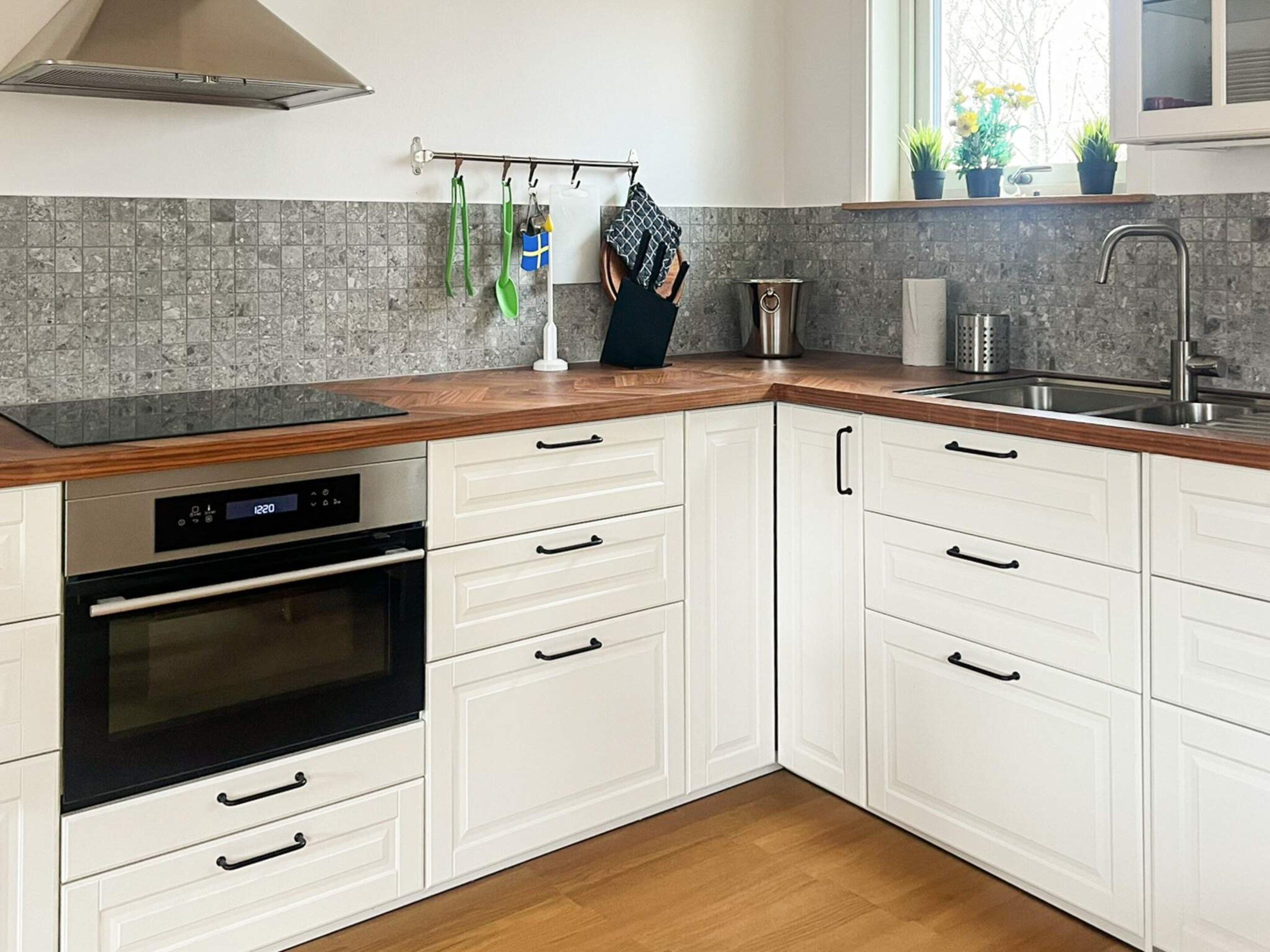 Una cocina moderna con armarios blancos, horno de acero inoxidable y encimera de madera.