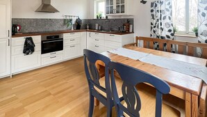Une cuisine moderne avec des meubles blancs, une table à manger en bois et une grande fenêtre agrémentée de rideaux à motifs floraux.