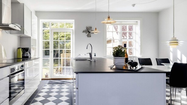A modern kitchen with a central island, a dining area with chairs, and a large window providing natural light. - 4 Star Holiday Home in Saeby (Sæby)