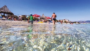 Een strandgezicht met helder ondiep water, parasols en mensen.