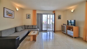 A modern living room with a sofa, a coffee table, a TV, and a sliding glass door leading to a balcony. - Cozy Beachfront Holiday Home Slatine (Split)