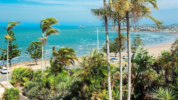 Blick auf die Küste mit Palmen, einem Strand und blauem Himmel.