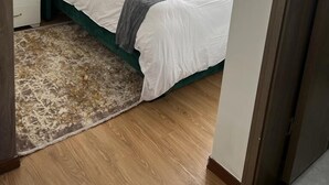 A neatly made bed with a green headboard, white bedding, and a grey throw blanket. - Vesta Garden Apartments Kilimani (Nairobi)