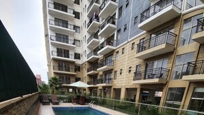 A swimming pool with a tiled deck, surrounded by a high-rise building with balconies. - Vesta Garden Apartments Kilimani (Nairobi)