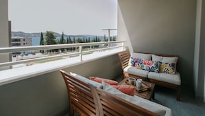 A balcony with a sofa and chairs, a view of the sea, and a building in the background. - Scenic Sea View Apartment Trogir (Seget)