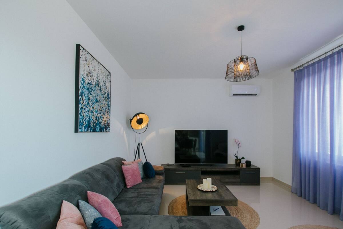 A modern living room with a grey sofa, a floor lamp, a flat-screen TV, and a coffee table.