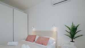 A modern hotel room with a bed, two pillows, a bedside table, a potted plant, and an air conditioning unit. - Scenic Sea View Apartment Trogir (Seget)