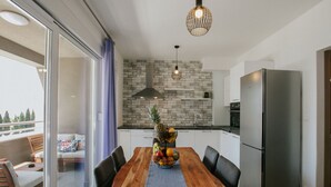 A modern kitchen with a wooden dining table, a fruit bowl, and a stainless steel refrigerator. - Scenic Sea View Apartment Trogir (Seget)