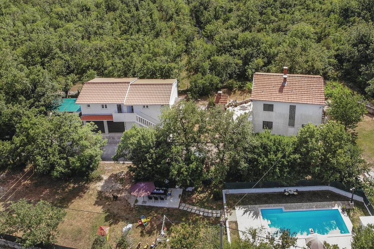 Two houses with red-tiled roofs surrounded by dense greenery.