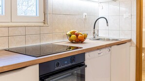 A modern kitchen with a built-in oven, a dishwasher, a sink, and a window with a view of bare trees. - Spacious Prgomet Retreat With Private Pool, Fitness Centre, and Garden (Prgomet)