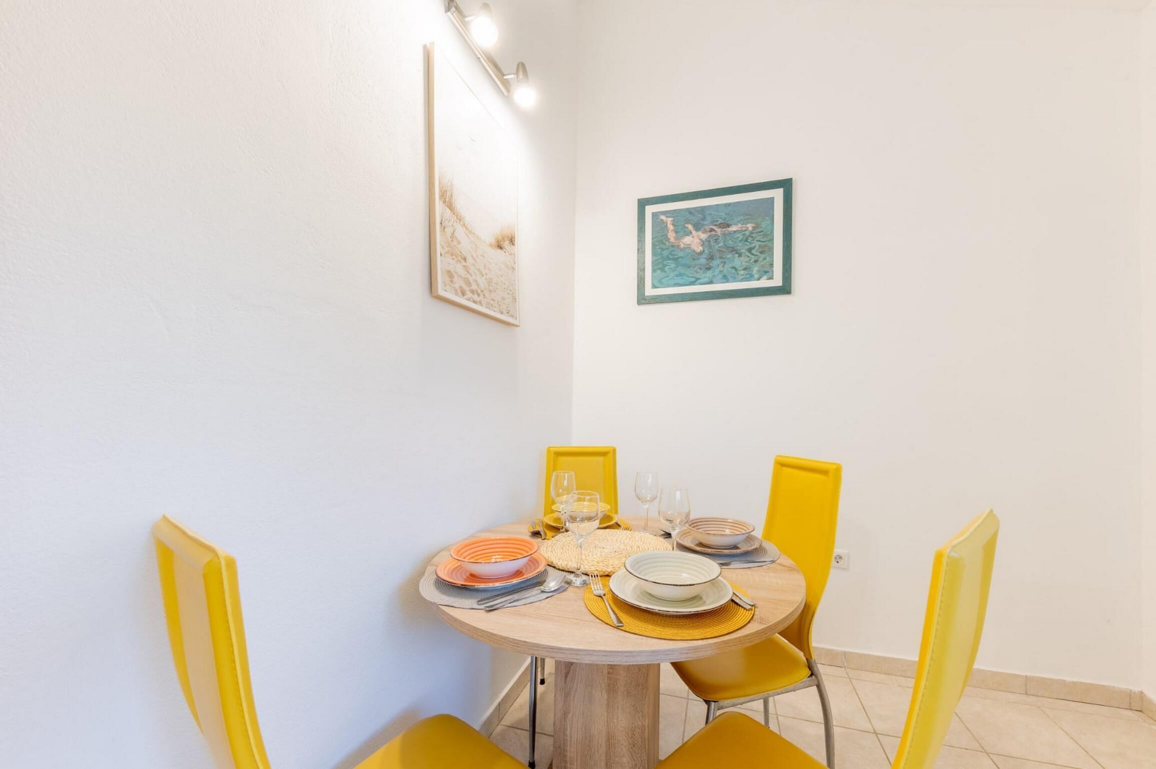 A dining area with a round table, yellow chairs, and a framed picture on the wall.
