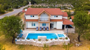 A two-story house with a swimming pool, stone walls, and a red-tiled roof.