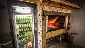 A kitchen with a brick oven, a refrigerator stocked with beverages, and a wooden table.