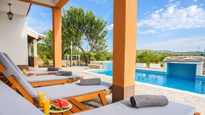 A poolside area with lounge chairs, a table with watermelon and drinks, and a view of the pool and landscape. - Secluded Holiday Home With Pool and Hot Tub (Lecevica)