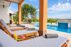 A poolside area with lounge chairs, a table with watermelon and drinks, and a view of the pool and landscape. - Secluded Holiday Home With Pool and Hot Tub (Lecevica)