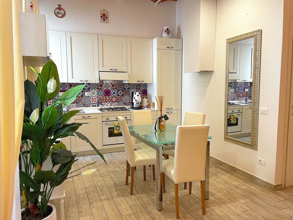 A modern kitchen with white cabinets, a glass dining table, and a large mirror. - My Luxury M&G Florence (Firenze)