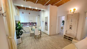 A spacious living area with a wooden ceiling, a dining table with chairs, a sofa, and a kitchen in the background.