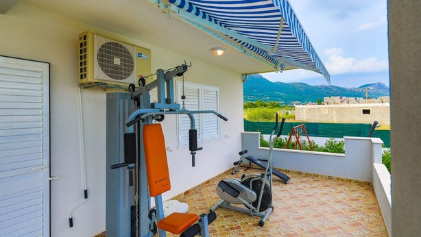 A covered outdoor gym area with exercise equipment, a large air conditioning unit, and a view of a mountainous landscape. - Family-friendly Holiday Home With Private Pool, Playground, and BBQ (Kastela)