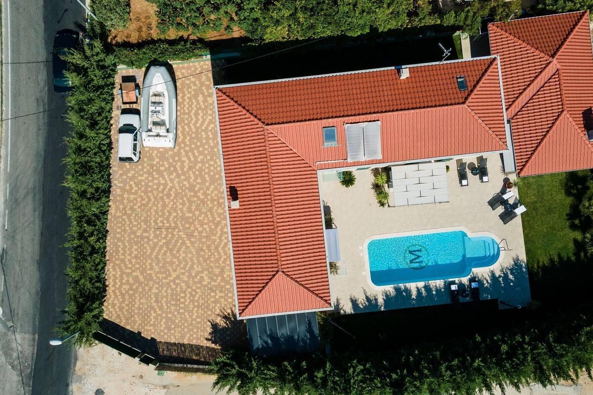 Luftaufnahme eines Anwesens mit Swimmingpool, Boot und einem Auto auf der Auffahrt.