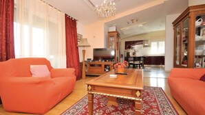 Ein Wohnzimmer mit zwei orangefarbenen Sofas, einem Holztisch, einem Fernseher und einer Kristallleuchter.