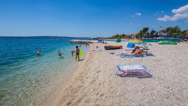 Ein Strand mit klarem Wasser, badenden Personen und Strandsonnenschirmen.