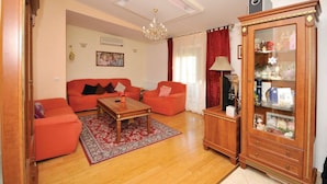 Ein Wohnzimmer mit zwei roten Sofas, einem Holztisch, einem roten Teppich, einer Holzkabine mit Glastüren und einer Kronleuchter.