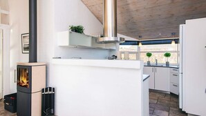 A modern kitchen with a built-in wood stove, white cabinetry, and a large window providing natural light. - 4 Star Holiday Home in Ronde (Ronde)