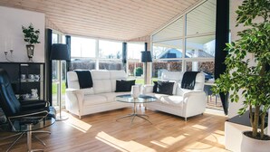 A modern living room with a white sofa set, a glass coffee table, and a black leather chair. There is a large window providing a view of the outdoors. - 4 Star Holiday Home in Ronde (Ronde)