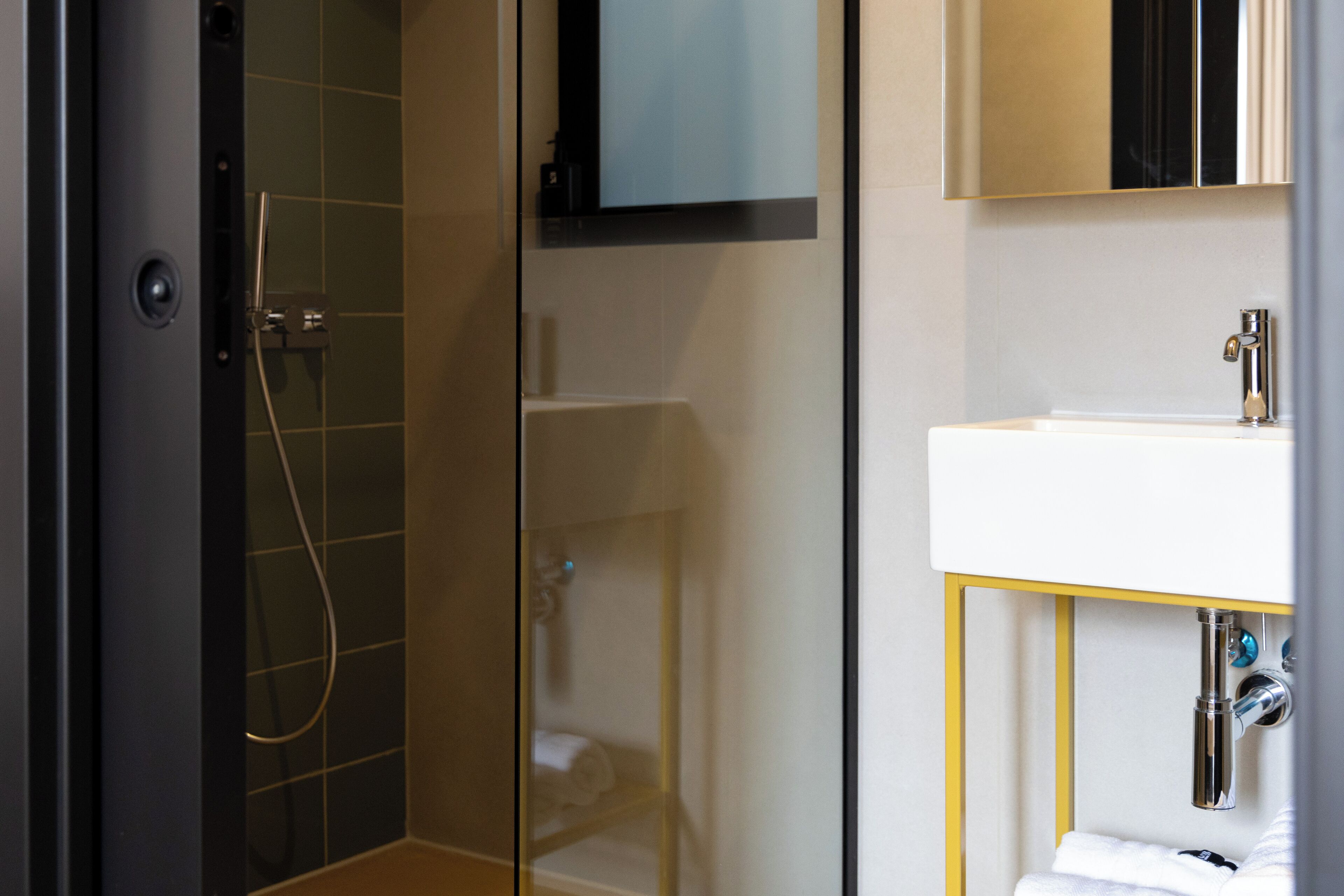Un baño moderno con ducha envuelta en vidrio, un lavabo blanco y un espejo sobre él.