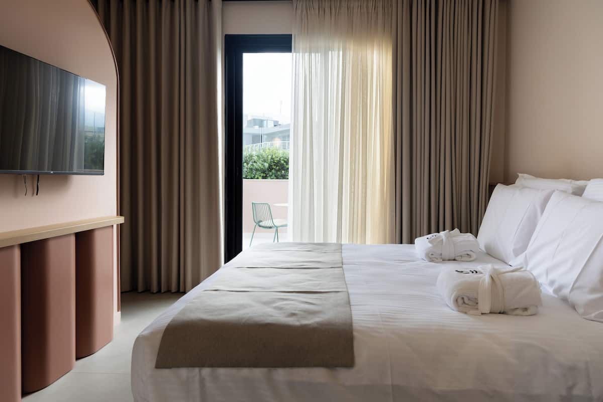 Ein Hotelzimmer mit Bett, einem an der Wand befestigten Fernseher und Blick ins Freie durch das Fenster.