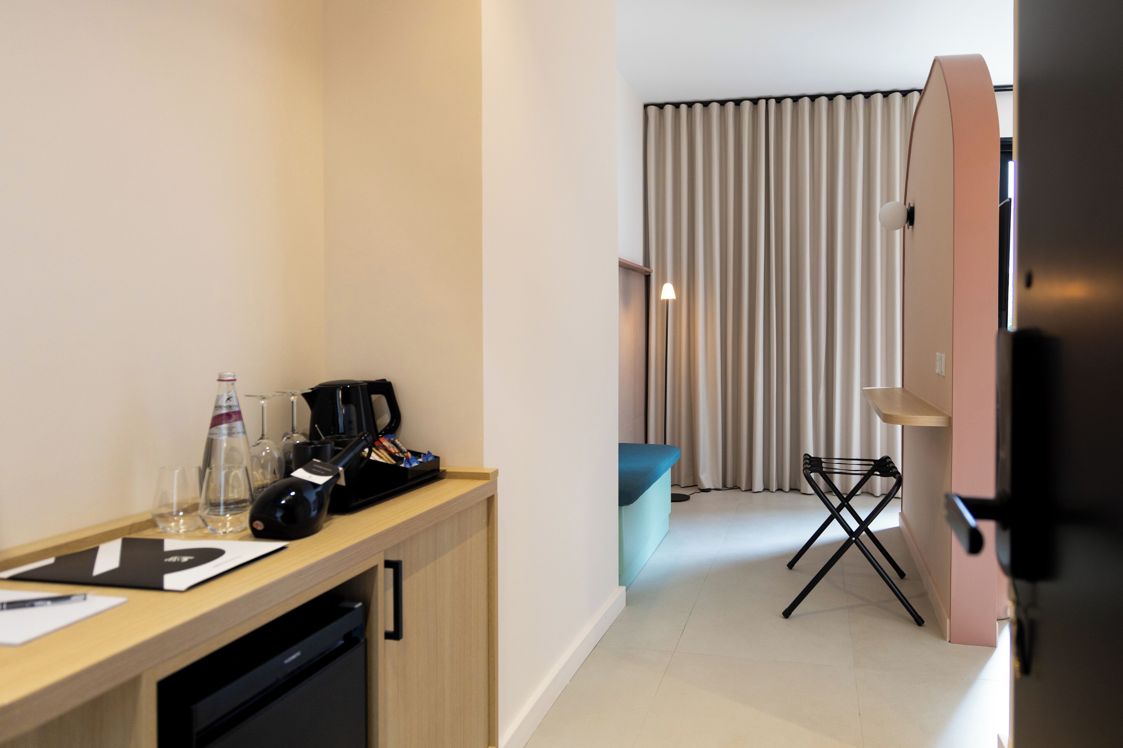 Ein Hotelzimmer mit Schreibtisch aus Holz, einer Kaffeemaschine und einer kleinen Sitzecke mit blauer Kissenlehne.