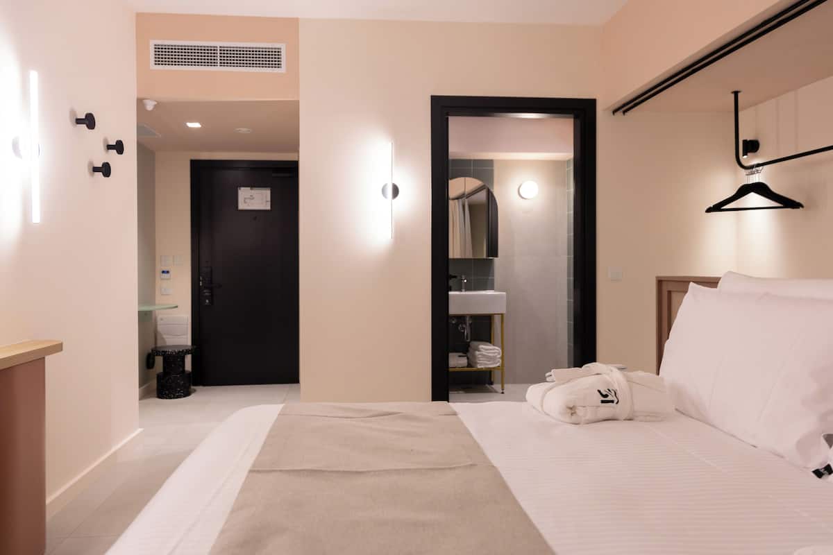 Ein Hotelzimmer mit einem Bett, einem Handtuch, einem Bademantel, einem Spiegel, einer Kleiderstange und einer Tür zu einem Badezimmer.