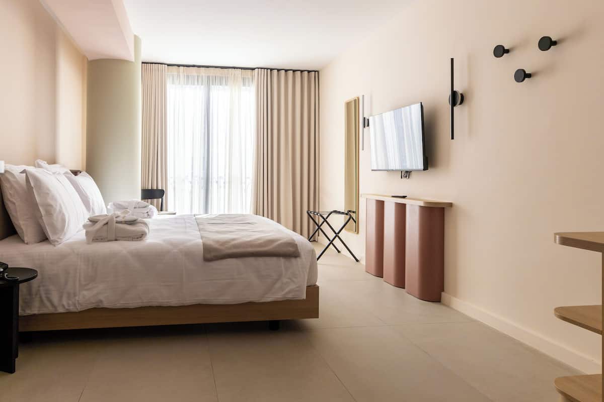 Ein modernes Hotelzimmer mit einem großen Bett, einem flachbildfernseher an der Wand und Blick auf die Stadt durch das Fenster.