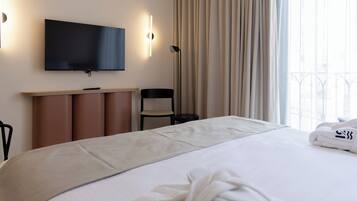 A hotel room with a large bed, a flat-screen TV mounted on the wall, a desk with a chair, and a window with curtains.