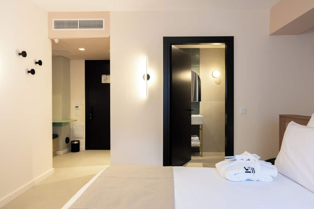 Ein modernes Hotelzimmer mit einem ordentlich bezogenen Bett, einem durchgegangenen Tür zu sehendem Badezimmer und einem kleinen Nachttisch.