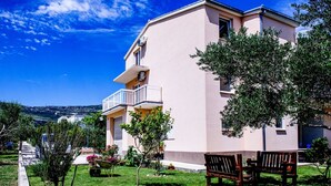 Ein zweistöckiges Gebäude mit Balkon, umgeben von viel Grün und blauem Himmel.