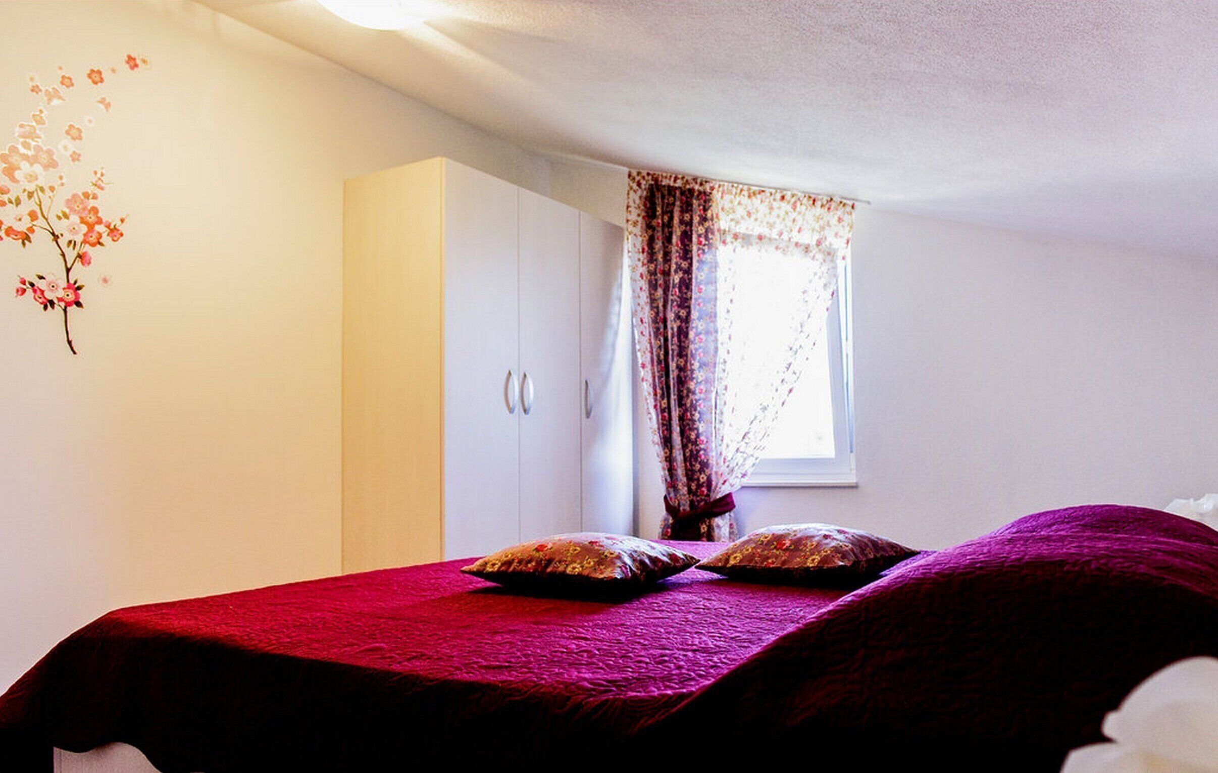 A bedroom with a bed, a wardrobe, and a window with curtains.