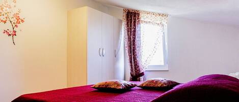 A bedroom with a bed, a wardrobe, and a window with curtains.
