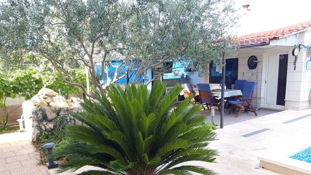 A pool area with a palm plant, outdoor seating, and a building with a tiled roof. - Kastel Stafilic Comfortable Apartments (Kastela)