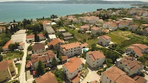 A residential area with multiple two-story houses, some with red-tiled roofs, surrounded by greenery and a body of water in the background. - Kastel Stafilic Comfortable Apartments (Kastela)