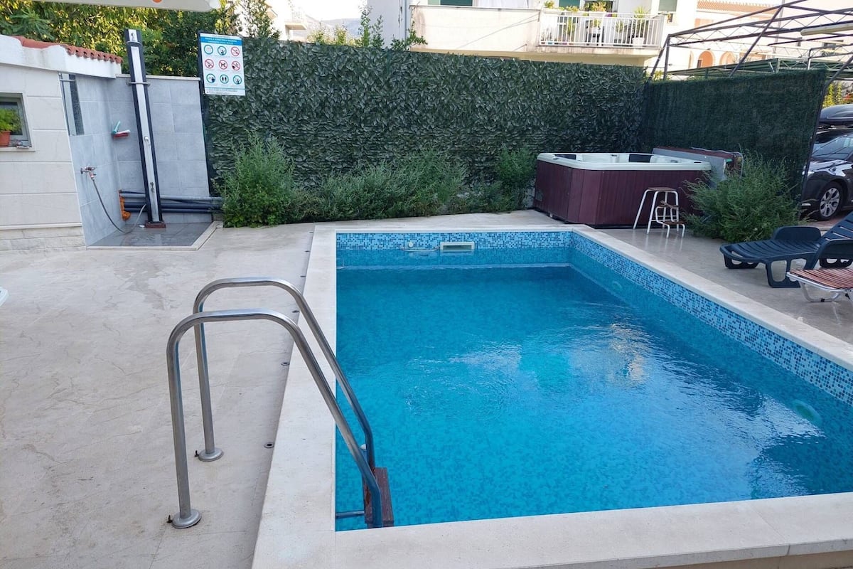 A rectangular swimming pool with a tiled edge, a metal ladder, and lounge chairs.