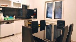 A modern kitchen with white cabinets, a black countertop, and a dining area with a glass table and black chairs. - Kastel Stafilic Comfortable Apartments (Kastela)