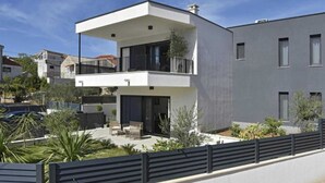 A modern two-story building with a balcony, a covered outdoor seating area, and a fenced garden. - Luxury Slatine Apartments With Terrace and Garden (Split)
